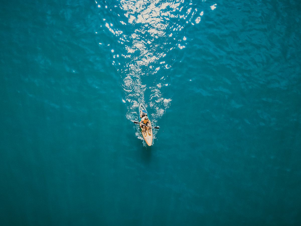 Aerial view of a single boat moving through clear blue waters, leaving a trail behind.