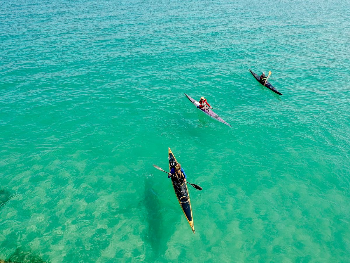 Three people are kayaking in clear, turquoise waters, viewed from above.