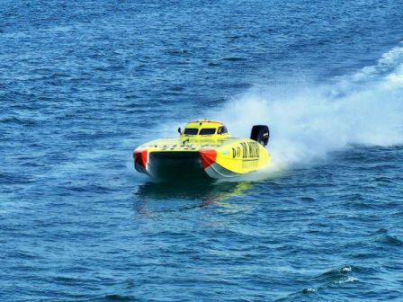 A bright yellow speedboat powers across blue water, leaving a white spray trail as it speeds along the surface.