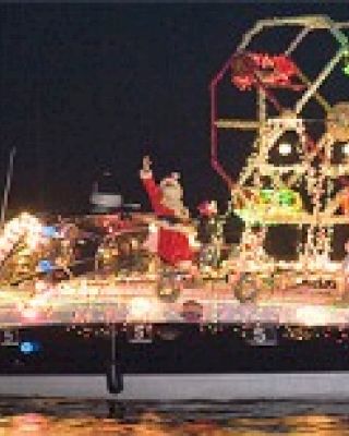 A boat decorated with colorful lights and festive figures, including a Santa Claus, floating on water at night, spreading holiday cheer.