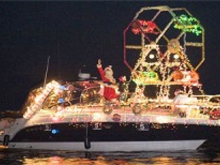 A boat decorated with colorful lights and festive figures, including a Santa Claus, floating on water at night, spreading holiday cheer.