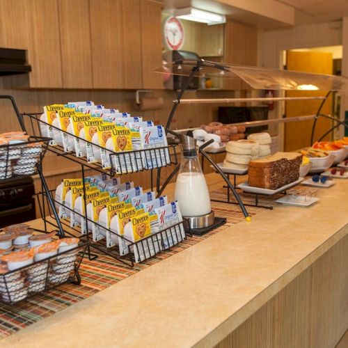 A hotel breakfast buffet with cereal boxes, milk, breads, and pastries arranged on long serving tables.