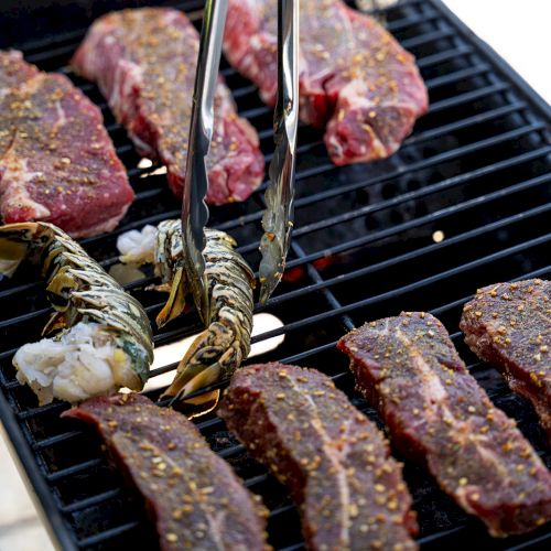 Grilling on a barbecue, showing seasoned steak cuts and shrimp on skewers sizzling on the grill grates.