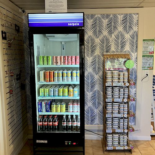 The image shows a refrigerator stocked with various beverages next to a display stand with assorted small items on it, against a patterned wall.