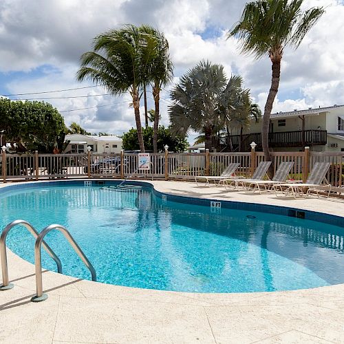 A sunny resort pool with palm trees, lounge chairs, and cabanas under a cloudy sky.