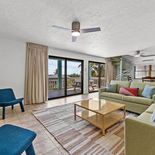 Bright living room with sofa, coffee table, rug, ceiling fan, and large sliding doors to a balcony.