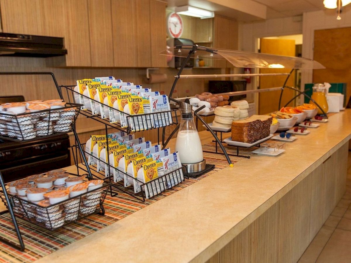 A hotel breakfast buffet with cereal boxes, pastries and fruits arranged on a counter under warm lights.