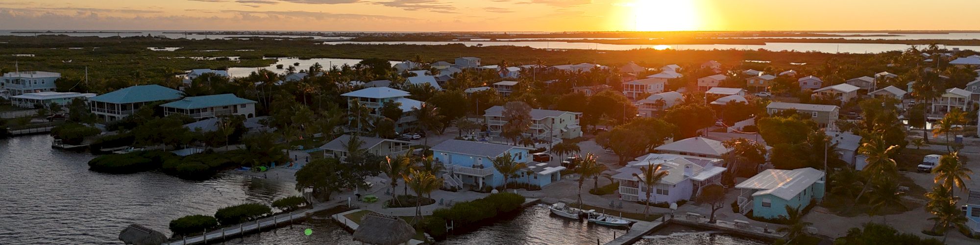 A serene sunset view over a coastal neighborhood with houses, docks, and calm water, creating a peaceful and picturesque scene.
