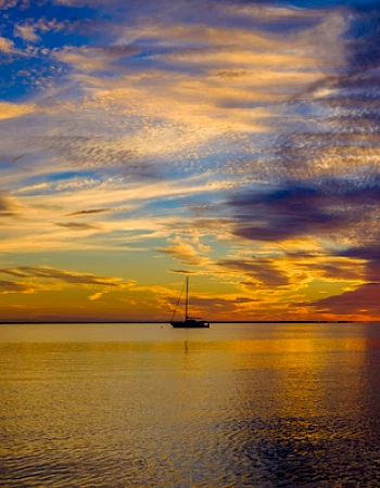 A sailboat on calm water during a colorful sunset with vibrant clouds in the sky.