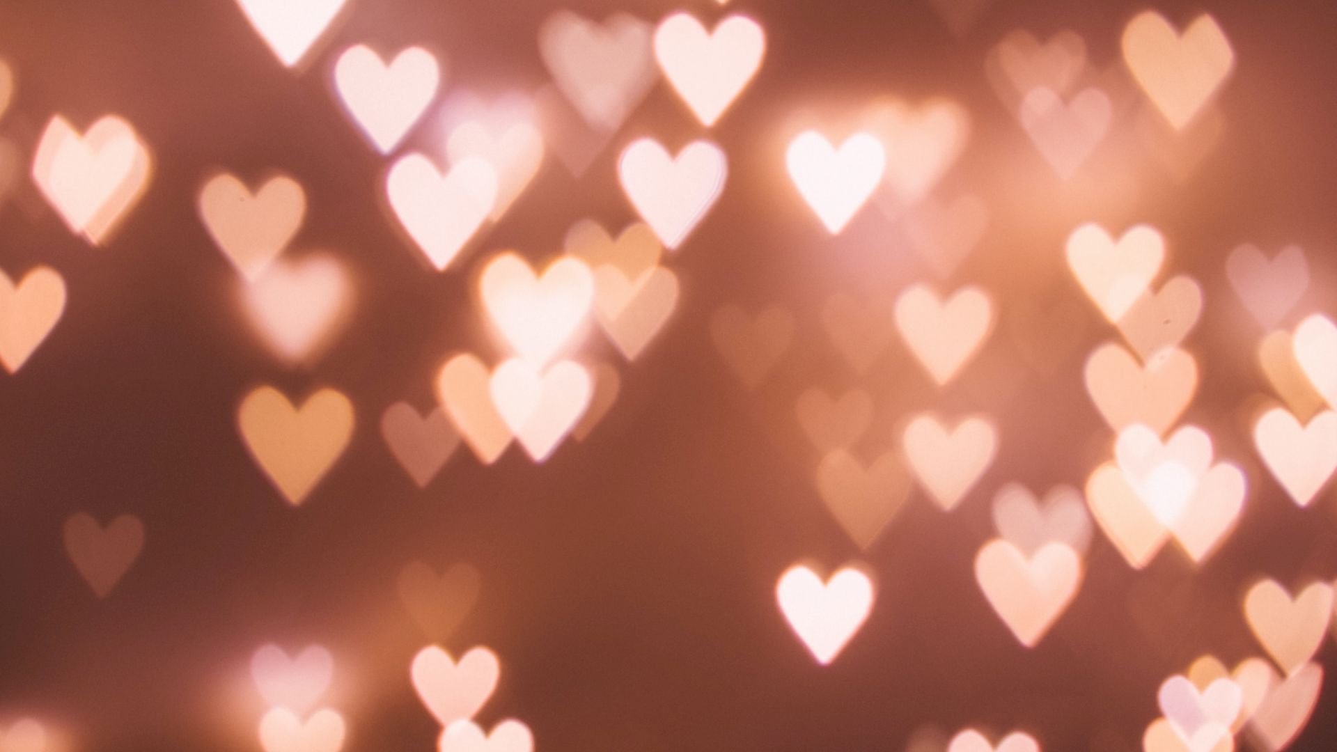 A dreamy background of warm bokeh heart shapes scattered across a soft brown-orange backdrop, like twinkling romantic lights.