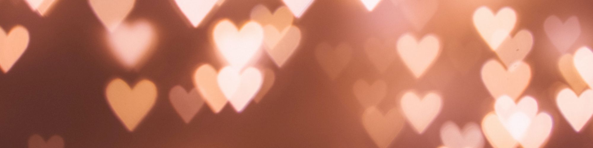 A dreamy background of warm bokeh heart shapes scattered across a soft brown-orange backdrop, like twinkling romantic lights.