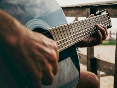 A close-up of a person strumming an acoustic guitar, focusing on the strings and frets as they play, outdoors on a sunny day.
