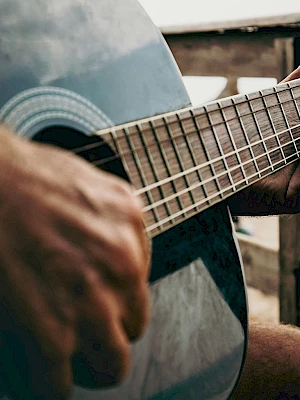 A person plays an acoustic guitar outdoors, close-up on fingers strumming the strings, wood grain and warm sunlight.