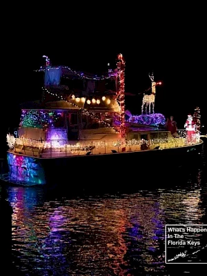 A brightly lit boat decorated with colorful Christmas lights glides on dark water, reflecting festive colors as silhouettes of figures stand aboard.