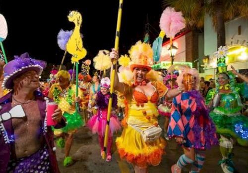 A vibrant carnival parade with performers in colorful feathered costumes and masks dancing in the street at night.