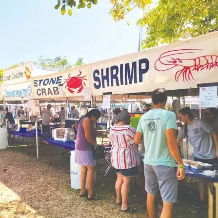 An outdoor seafood stand selling shrimp and crab, with big signs and people browsing tables on a sunny day.