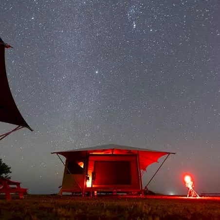 A red-lit telescope/camera rig under a starry night sky with bright stars and a glowing observer.