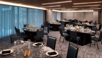 The image shows a banquet hall setup with round tables, black chairs, elegant table settings, candles, and flower centerpieces.
