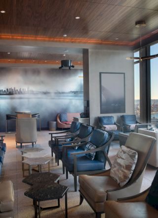 A modern lounge with multiple chairs, a city mural on the wall, and large windows offering a view of water and a Ferris wheel.