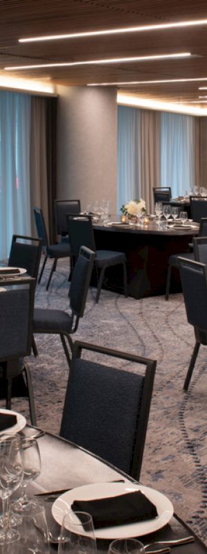 A banquet hall with round tables set for a formal event, featuring elegant place settings, black napkins, and floral centerpieces on the tables.
