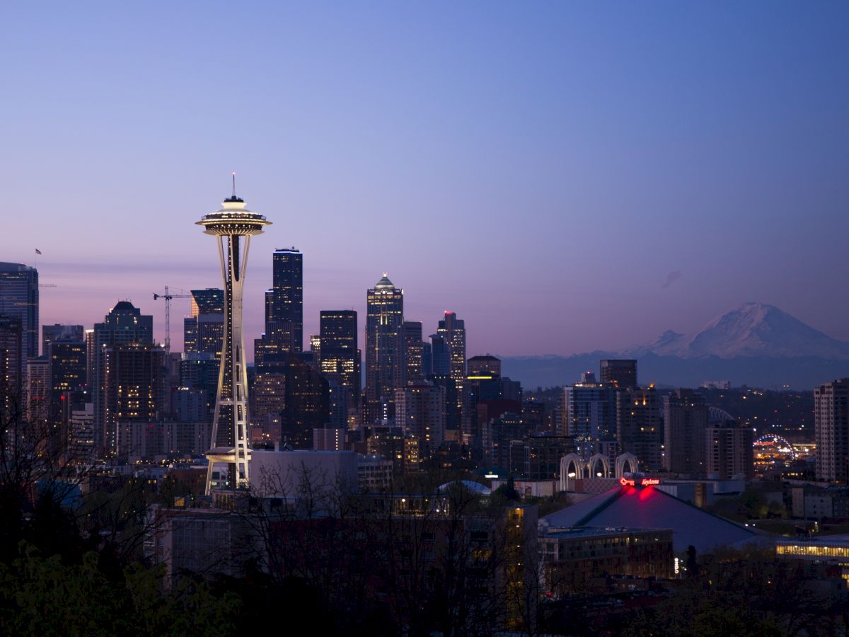 A twilight view of Seattle's skyline with the Space Needle prominently in the center, featuring nearby buildings and a mountain in the background.