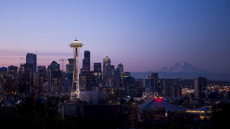 A twilight view of Seattle's skyline with the Space Needle prominently in the center, featuring nearby buildings and a mountain in the background.