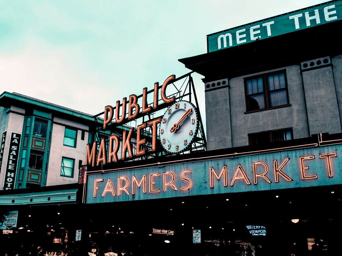 The image shows a public market building with neon signs reading "Public Market" and "Farmers Market." A clock is also visible in the center.