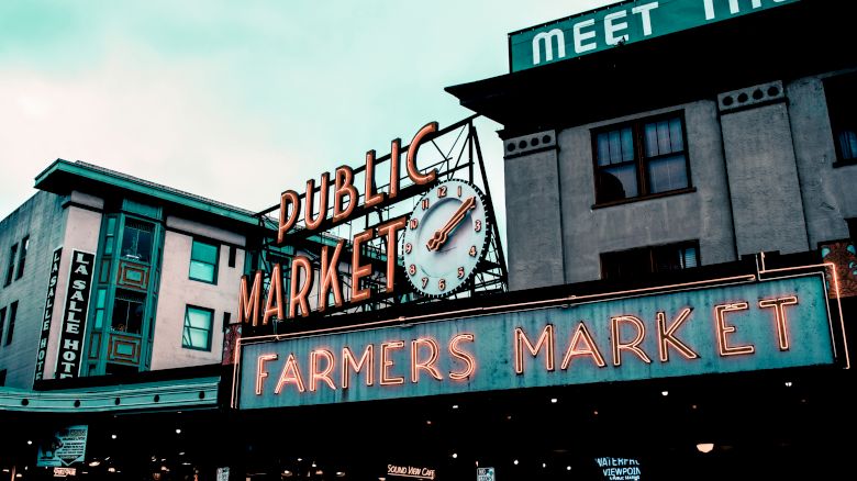 The image shows a public market building with neon signs reading "Public Market" and "Farmers Market." A clock is also visible in the center.
